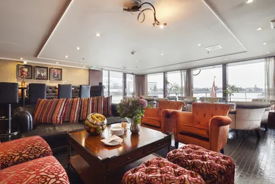 Die Captain's Corner auf dem Flusskreuzfahrtschiff MS Antonio Bellucci von Thurgau Reisen. Der gemütliche Raum ist mit bequemen Sitzgelegenheiten und maritimer Dekoration gestaltet. Hier können Passagiere entspannen und den Blick auf den Fluss genießen, während informative Ausstellungen über das Schiff und die Reise angeboten werden.