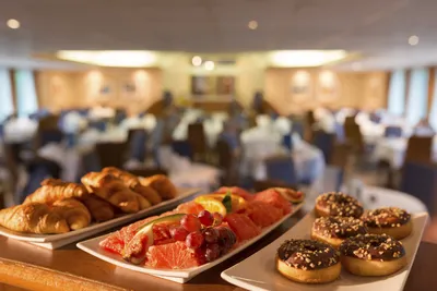 Ein Buffet auf dem Flusskreuzfahrtschiff Seine Comtesse von Thurgau Reisen, das eine Auswahl an frischen Croissants, Obst und Donuts präsentiert. Im Hintergrund sind die elegant gedeckten Tische des Essbereichs sichtbar, die eine einladende Atmosphäre schaffen.