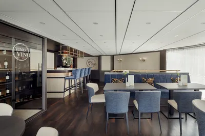 Die Lido-Bar auf einem Flusskreuzfahrtschiff Scilly Gloria von Thurgau Reisen. Der elegante Raum verfügt über eine moderne Einrichtung mit blauen Stühlen und Tischen. Im Hintergrund ist die Bar mit einer Auswahl an Getränken sichtbar, während große Fenster für viel Tageslicht sorgen.
