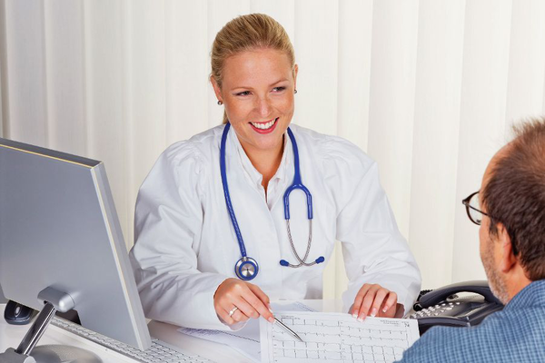 Ein Schiffsarzt in einem modernen Büro spricht freundlich mit einem Patienten. Die Ärztin trägt einen weißen Kittel und ein Stethoskop. Im Hintergrund ist ein Computer zu sehen, was die medizinische Umgebung an Bord eines Flusskreuzfahrtschiffs von Thurgau Reisen verdeutlicht.