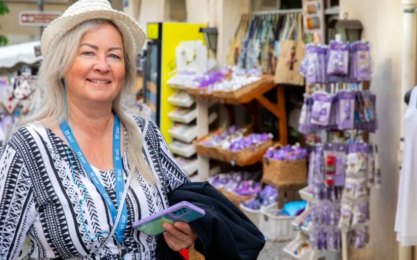 Eine Passagierin von Thurgau Reisen beim Landgang in Avignon. Sie trägt einen Strohhut und lächelt, während sie in einem kleinen Markt mit bunten Souvenirs und lokalen Produkten steht. Im Hintergrund sind Regale mit Lavendel und anderen typischen regionalen Artikeln zu sehen, die die charmante Atmosphäre der Stadt unterstreichen.