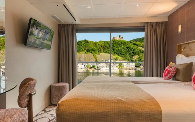 Kabine der MS Edelweiss mit Panoramafenster und französischem Balkon mit Ausblick auf Stadt am Flussufer.