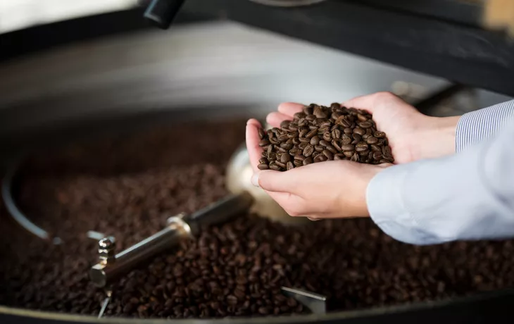 © contrastwerkstatt - stock.adobe.com - Frau in der Rösterei hält Kaffeebohnen in der Hand