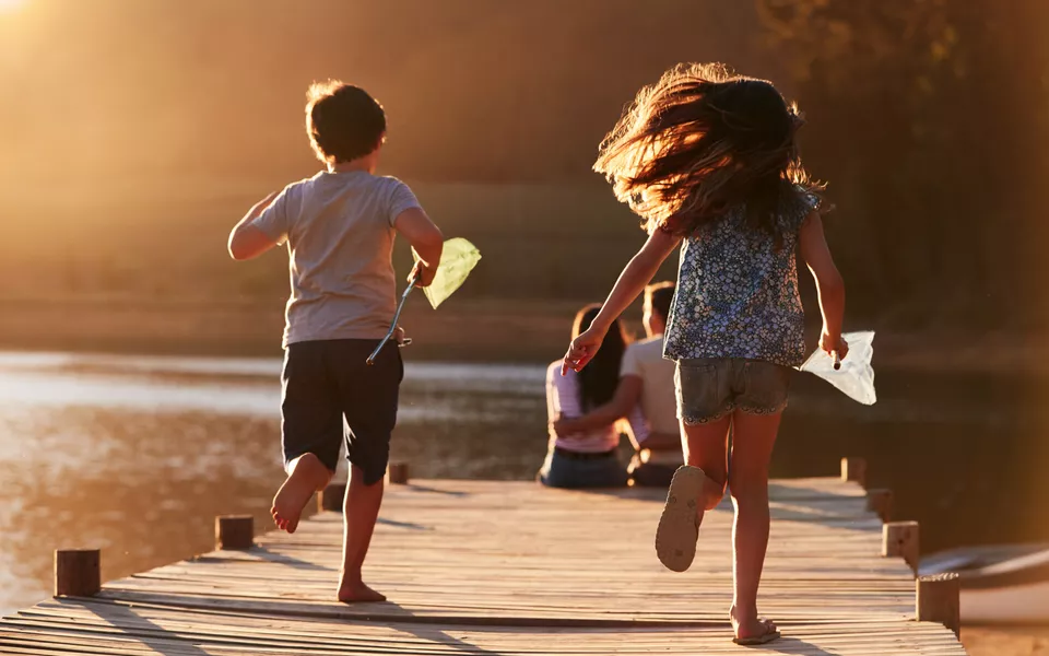 Kinder laufen auf hölzernen Steg am See auf Eltern zu